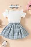 A sweet ensemble of new born cloths for a baby girl: a white bodysuit with a teddy bear, a blue plaid skirt, and a headband, reflecting current trends in girls fashion. While the top is a bodysuit, the overall look could be considered a type of romper dress.
