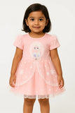A young girl with short dark hair smiles, wearing a short-sleeved white top with a subtle floral print and a rounded collar underneath an olive green overall dress. The dress has a cream-colored bib pocket with embroidered pink cherries. This is a charming piece of girls kids clothing and trending clothes for girls, showcasing a sweet style in girls fashion. It's a lovely dress for kids girls.