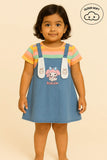 "Girls kids clothing featuring a young girl wearing a colorful striped t-shirt and a blue denim pinafore dress with cartoon characters on the straps and front, showcasing girls fashion, girls wear, and trending clothes for girls."

