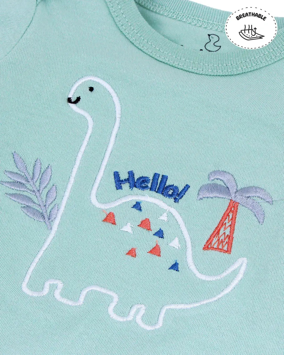 Light green fabric with an embroidered dinosaur, palm tree, and the word 'Hello!' in blue text. The dinosaur has colorful triangular patterns on its body.