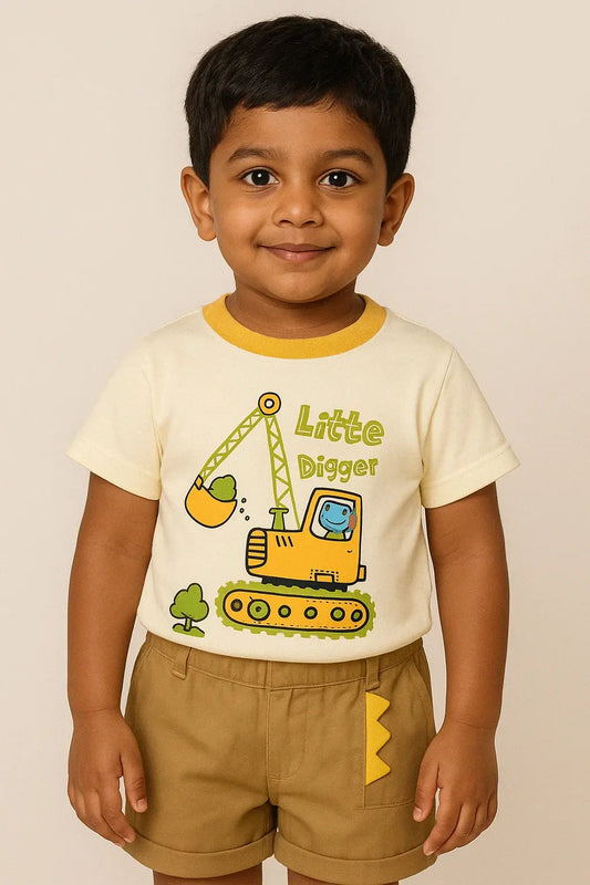 A young boy with dark hair smiles while wearing a cream-colored short-sleeved t-shirt with a yellow trim and a cartoon excavator graphic that reads "Little Digger." He is also wearing khaki shorts and standing against a light beige background.